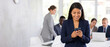© Five Million Stock - Smiling latin Hispanic young female businesswoman ceo manager working on smartphone with people on background. European business woman trader using cell phone mobile trade online in office. Copy space