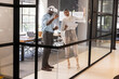 © wavebreak3 - Diverse coworkers standing near glass board in office, using vr gear holding printed plans