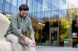 © Liubomir - Man sitting on a bench outdoors experiencing intense knee pain, holding his injured joint with hands, indicating discomfort, health problem, and an urgent need for medical help