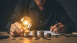 © NASRINAHAKIM - Man with a bright idea brainstorming and calculating finances with coins and a lit bulb