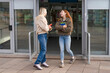 © Iryna - Two friends meet outside a building and engage in conversation while holding books