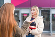© Iryna - Two students talk outside a building during the day while holding books in their hands
