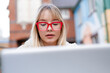 © Iryna - Young woman works on laptop in outdoor setting during the day near colorful buildings