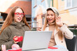 © Iryna - Friends enjoy a sunny day sharing laughs while working on a laptop at an outdoor cafe