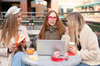 © Iryna - Friends gather outdoors to work on a laptop and enjoy coffee on a sunny day in a city