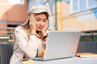 © Iryna - Woman sitting outside, working on laptop while looking stressed in urban area
