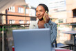 © Iryna - Woman talking on phone while working at outdoor table with laptop in busy urban area