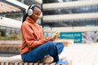 © Iryna - Young woman listens to music while using phone outdoors in a modern urban setting
