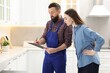 © New Africa - Young woman and plumber with clipboard signing documents in kitchen
