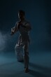 © New Africa - Man in uniform practicing karate on dark light blue background with smoke