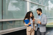 © Novak - Businessman and businesswoman standing in front of a modern office building, discussing a project using a digital tablet and paper documents