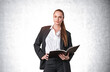 © ImageFlow - Businesswoman in suit holding open notebook, professional style, standing against a light textured background, concept of leadership and planning