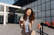 © Novak - Professional businesswoman holding a digital tablet and a takeaway coffee cup standing in front of a modern office building