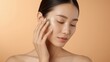 © LimeSky - Young woman using a jade gua sha tool on her face against a light orange backdrop.png