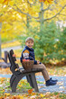 © Tomsickova - Cute little child, sweet boy in a park, sitting on a bench and in the foliage, eating apple, smiling and playing with leaves