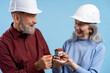 © Maria Vitkovska - Smiling senior coworkers wearing white hard hat holding cute mini house project, talking