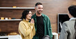 © wedmoments.stock - Smiling couple in casual attire standing in a modern kitchen with wooden accents, engaging with a realtor during a property showing in a bright and inviting atmosphere