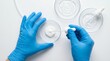 © Norah Allen - Hands wearing blue protective gloves carefully applying clear liquid serum from a dropper onto a white cream sample in a petri dish during cosmetic testing laboratory skincare research