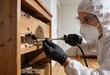 © Netsai - Pest control technician in protective gear spraying insecticide into a severely termite-infested wooden cabinet indoors.