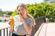 © luismolinero - Young blonde woman holding an orange juice at outdoors whispering something
