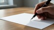 © Adeel - Close-Up of a Hand Writing with a Pen on Blank White Paper on a Wooden Desk