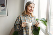© shurkin_son - Senior lady checking her mobile app on smartphone holding cup of coffee and admiring winter city panorama through big window of her living-room, making taxi request online via application
