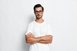 © SHOTPRIME STUDIO - Confident young man stands with crossed arms, wearing a white t-shirt and glasses, looking thoughtfully at the camera against a neutral background.