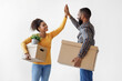 © Prostock-studio - Happy millennial black couple carry cardboard boxes with potted plant, give high five on white wall background. Excellent purchase of apartment, relocation and positive emotions of home owners, indoor