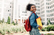 © Prostock-studio - Happy African American Student Girl Posing With Backpack Holding Books Smiling Looking Aside Standing Near University Building Outdoor. Modern Education And Studentship Lifestyle