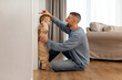 © Home-stock - Loving father measuring height of little daughter next to white wall, holding hand over kids head, light living room. Growth Tracking Time