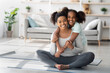 © Prostock-studio - Sporty black mother and daughter sitting on fitness mat, hugging and smiling, home interior. Happy african american parent and girl kid in sportswear having moring training together in living room