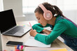 © Prostock-studio - Side view profile of focused little girl writing down information watching webinar on laptop with empty screen or taking notes in her diary, wearing wireless headphones, pc with free space mock up