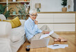 © Lumos sp - Portrait of a senior woman working on laptop sitting on the floor at home