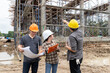 © skarie - Team of civil engineers and architects discussing construction plan with blueprint and pointing at scaffolding structure.