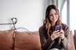 © luciano - Portrait of smiling woman in video call to friends or relatives, using phone webcam, sitting on couch at home, happy young female blogger recording vlog, chatting online