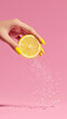 © Anna - A hand with yellow nails squeezes a lemon slice, releasing droplets of water against a pink background. Perfect for food and beverage themes.