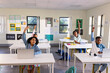 © Wavebreak Media - Teenage classmates raising hands at desks in classroom with laptops, pi poster, headphones