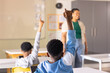 © Wavebreak Media - African American boy sitting at desk wearing blue sweatshirt, raising right arm toward whiteboard