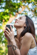 © aFotostock - Vertical Horizon Woman drinking coffee hands holding hot disposable cup in green park. Vertical Happy Relax beautiful asian woman smiling face standing outdoors garden. Women enjoy nature Lifestyle