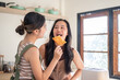 © bongkarn - Happy asian woman feeding a toasted bread to girlfriend while standing aside kitchen cooking counter