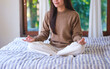 © Farknot Architect - Closeup image of a young woman meditating or practicing yoga in lotus pose on the bed