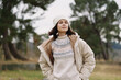 © SHOTPRIME STUDIO - Woman in a beige coat and knit sweater stands outdoors in a park, wearing a knit beanie, conveying casual fashion and cozy warmth during a chilly day in nature