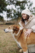 © SHOTPRIME STUDIO - Woman in winter coat and knit hat smiles as she pets a brown and white dog outdoors in a park, capturing warmth, companionship and gentle contact with a loyal pet