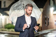 © Volodymyr - Night business. Businessman talks on his phone under an umbrella on a rainy night. Manager makes a business call in the rain. Man in suit phone phone in night street. Business man checks schedule.