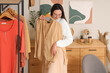 © Pixel-Shot - Young woman trying on blouse near clothes rack at home