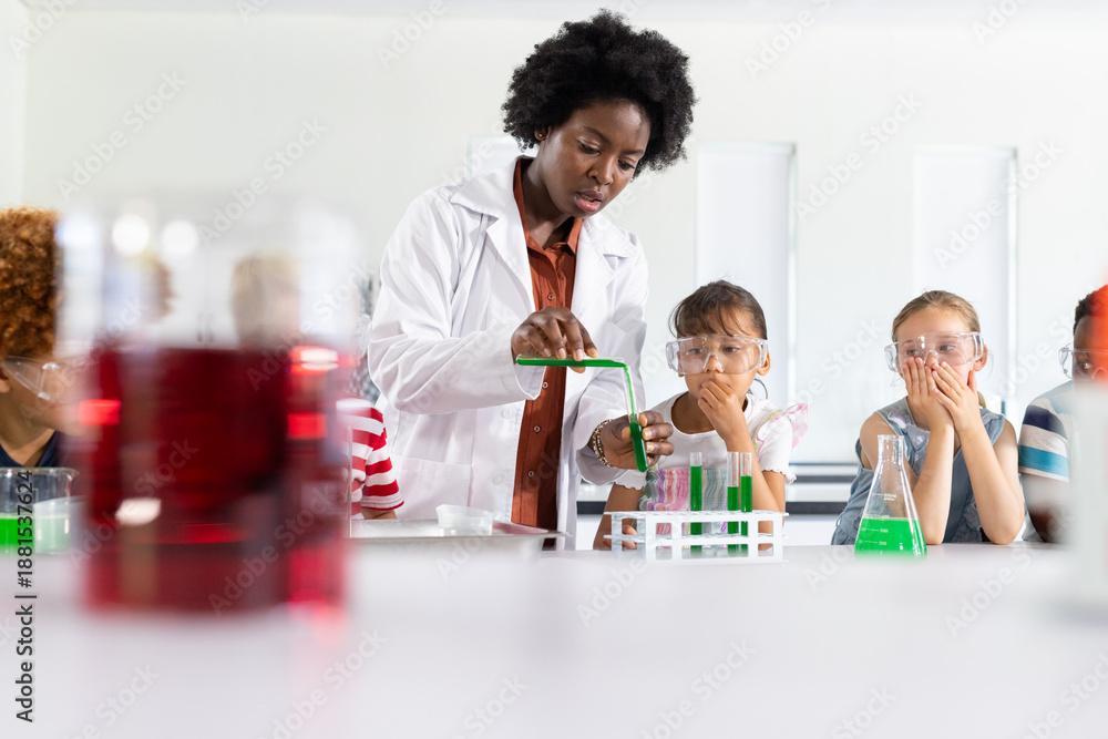 African American woman in white labcoat pouring liquid into test tube ...
