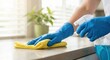 © Gayan - Close up of an adult White woman wearing blue gloves cleaning and sanitizing a countertop with a yellow cloth and spray bottle in a bright home interior during the morning