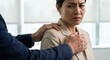 © Gayan - Adult Southeast Asian woman feeling anxious and uncomfortable as a male colleague places hands on her shoulders in a bright office, concept of workplace harassment and unwanted touch.