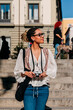 © Westend61 - Tourist holding camera on steps outdoors in Madrid on a sunny day