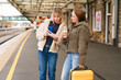 © Iryna - Friends check phone at train station while waiting for departure with suitcase and coffee